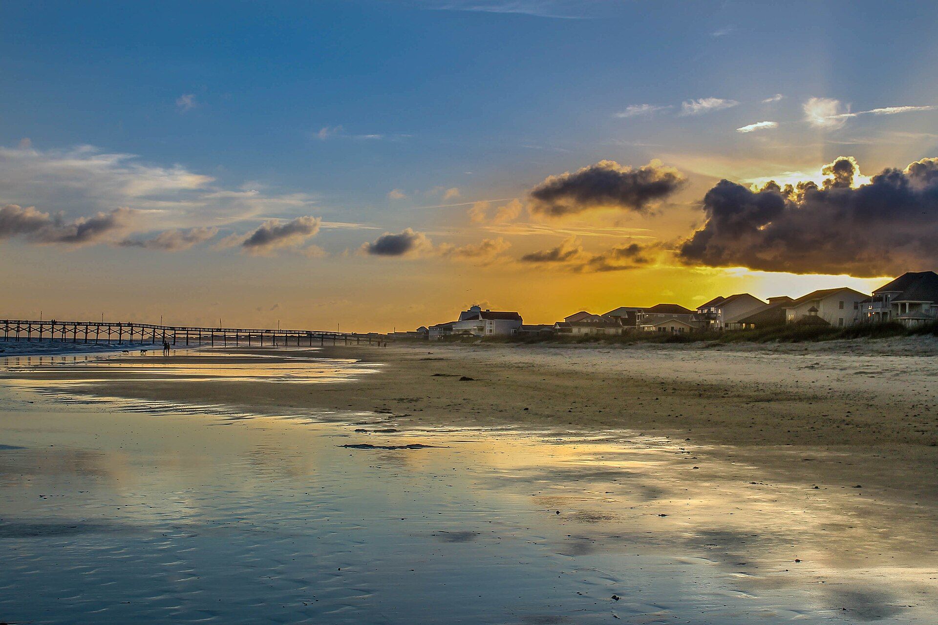 Sunset over the beach at Oak Island, NC, with the Oak Island Pier in the distance and the sky reflected on wet sand